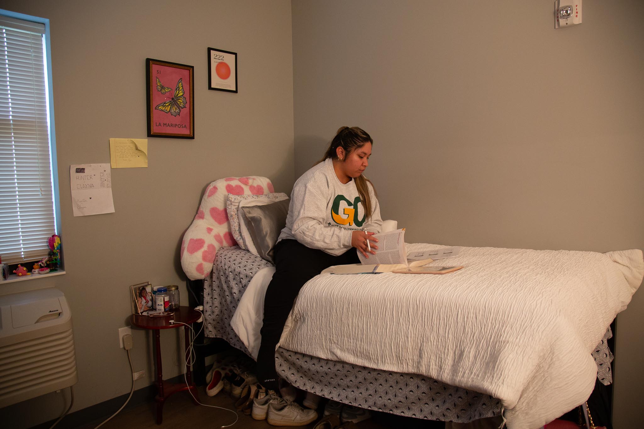 female student sitting on a twin bed in her student housing unit studying