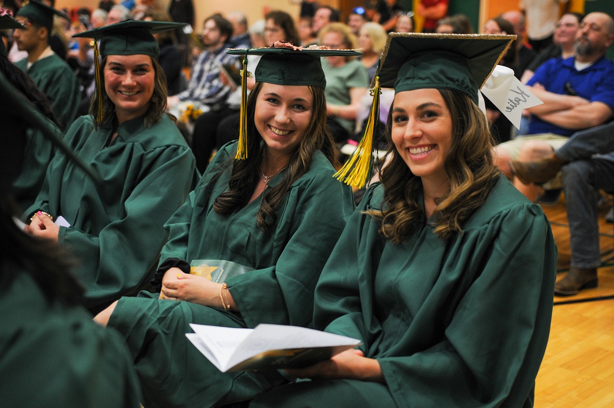 3 female friends wearing caps and gowns sitting at graduation