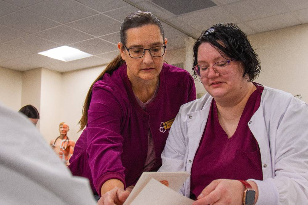 Allied Health Instructor talking with students, standing over her shoulder, showing her papers