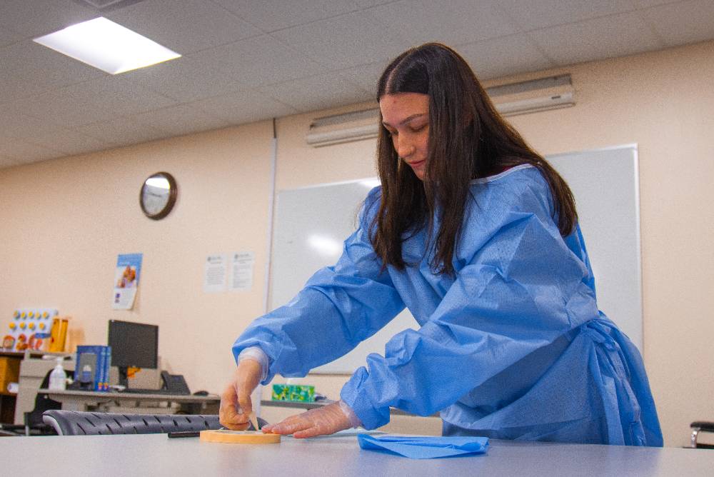 Student in scrubs assisting with testing devices.