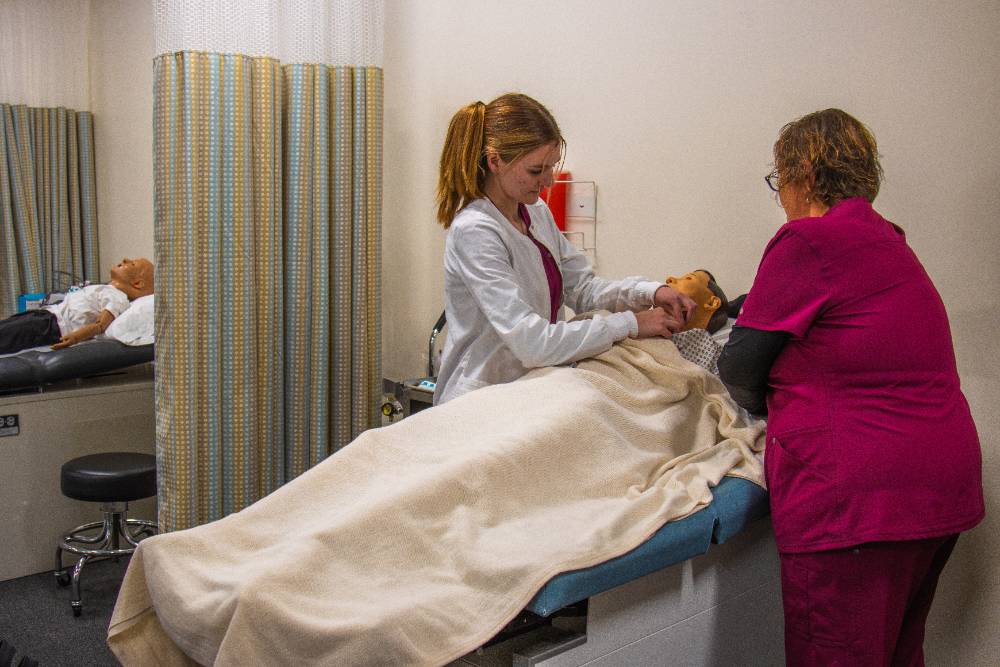 Two allied health students assisting a patient in bed. 