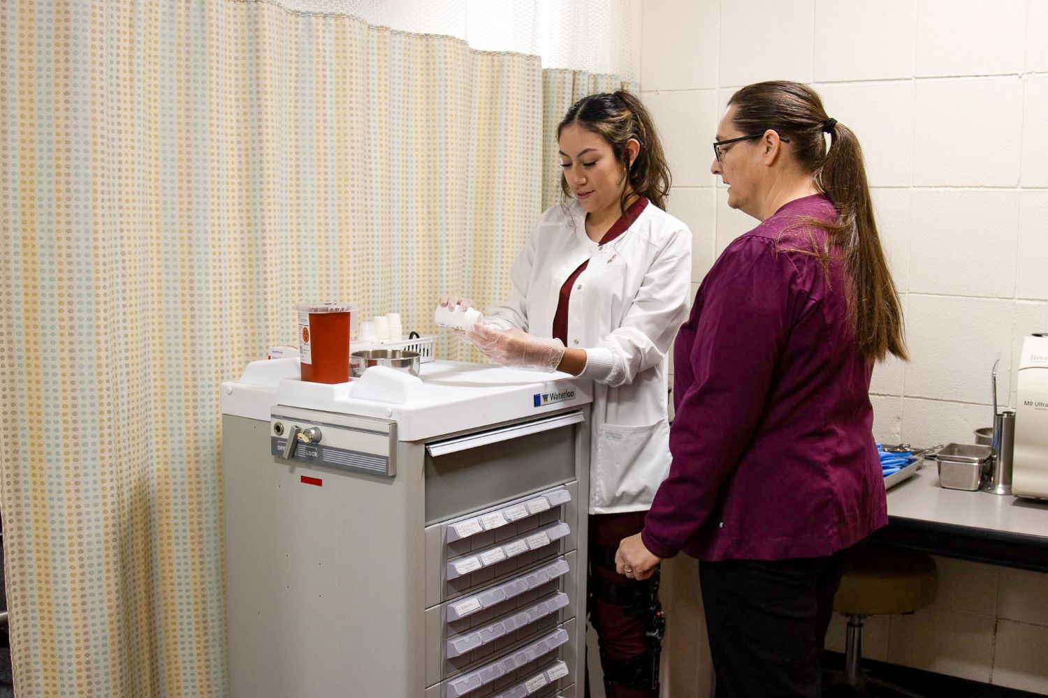 Allied Health students standing at a medical cart with her instructor reviewing medication