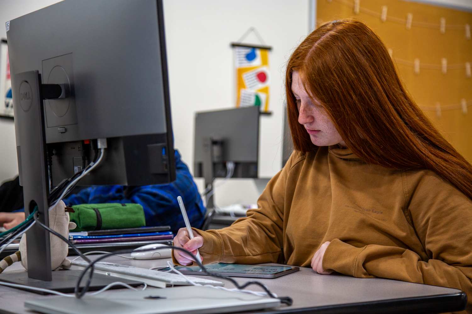 Students sitting in front of computer screen drawing on design tablet