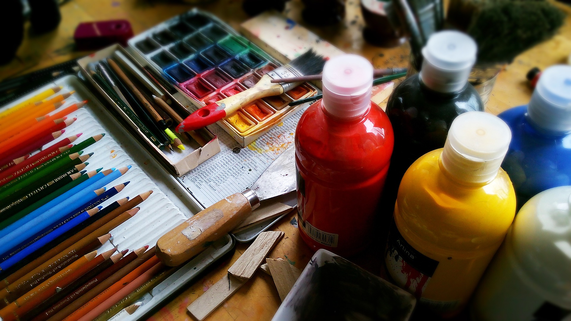 colored pencils, artist paint and brushes on a table.