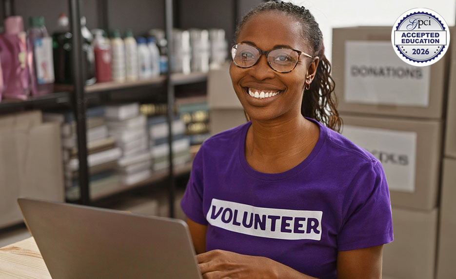 Female smiling at camera, sitting in front of a laptop with file cabinets behind her