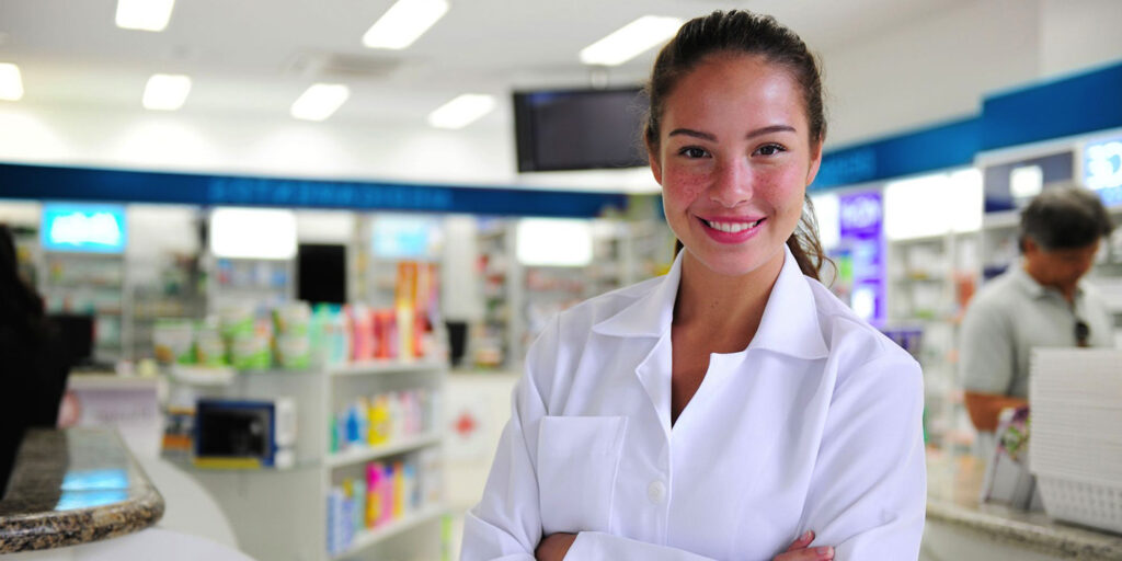 Female pharmacy technician in white coat standing in pharmacy.