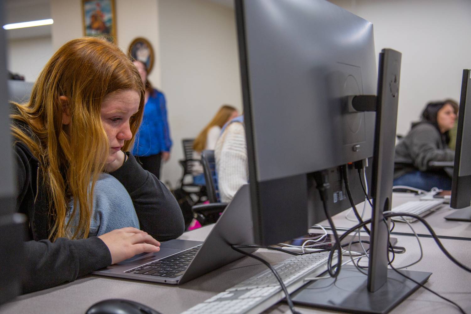 Red-headed female student sitting at laptop in front of class.