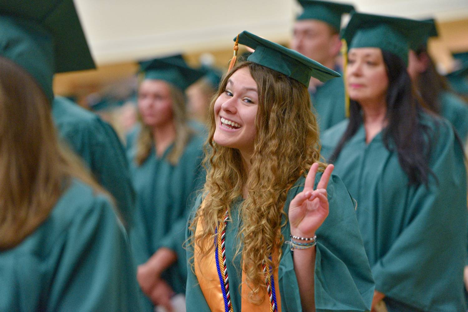 Female GOCC student in cap and gown at graduation flashing a peace sign.